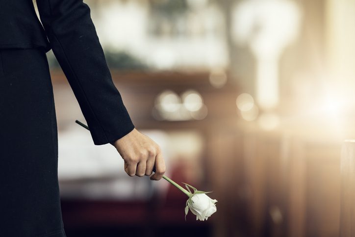 Hand holding white rose in memorial setting